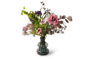 Kunstbloemen gepresenteerd in grote glasvaas in de kleur blauw. Boekt heeft de kleuren grijs, lila en paars en bevat Lisionthus, Agapanthus,  Bes en diverse andere