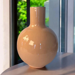 Sfeerfoto Bolvormige vaas 23x30cm in een honing kleur met een glanzende afwerking diameter boven 7,5cm op een houten tafel voor het raam - WinQ