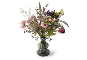 Diverse kunstbloemen waaronder pioen, Lavendel' scabiosa en distel gebonden en gepresenteerd in een blauwe glasvaas