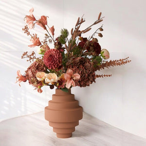 Boeket kunstbloemen met opgeruwde oud roze metalen vaas op een een lichte houten houten tafel in een kamer