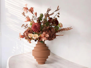 Boeket kunstbloemen met opgeruwde oud roze metalen vaas op een een lichte houten houten tafel in een kamer