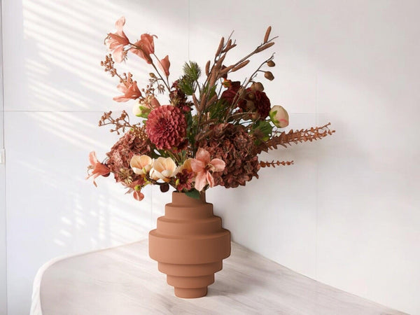 Boeket kunstbloemen met opgeruwde oud roze metalen vaas op een een lichte houten houten tafel in een kamer